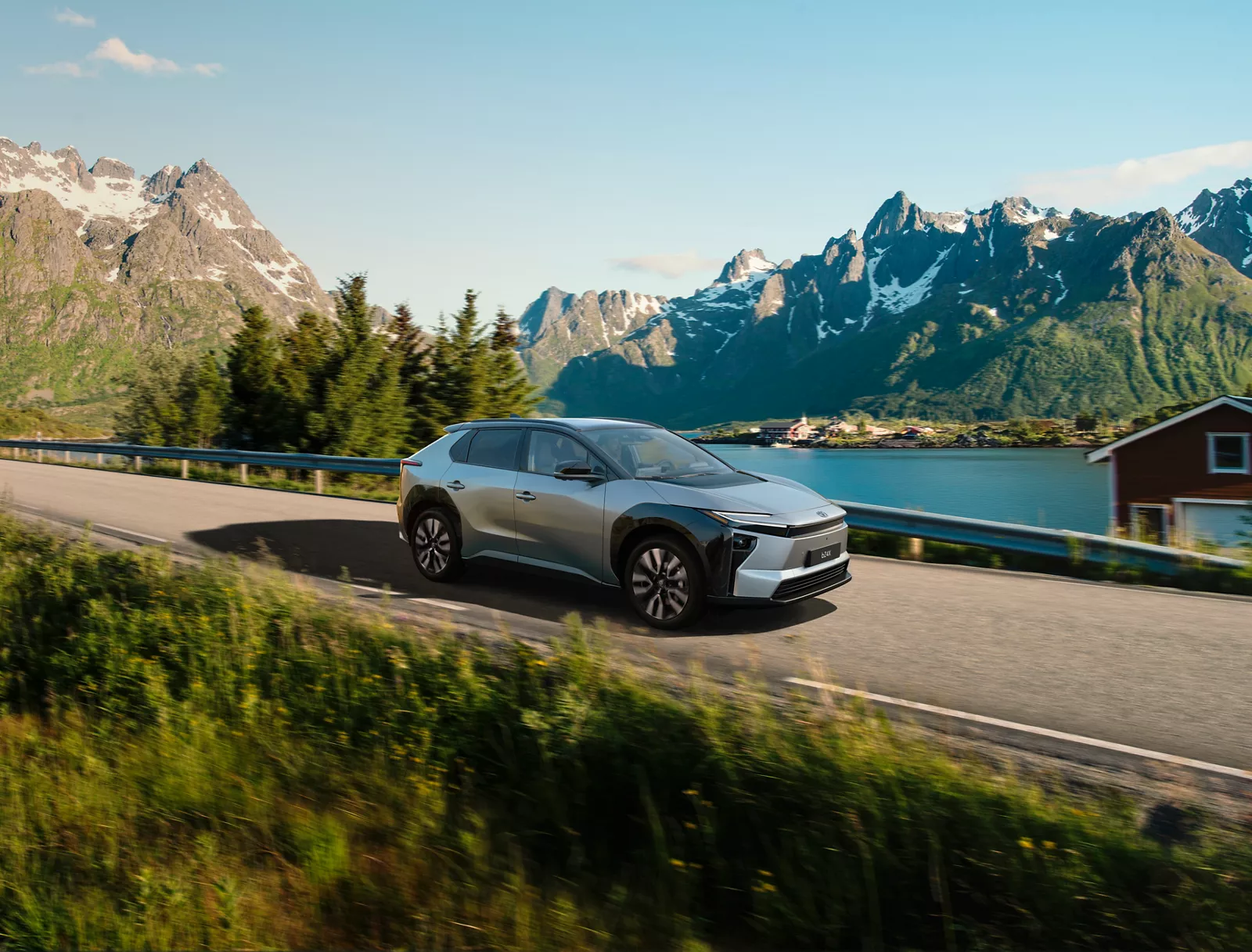Silberner überarbeiteter Toyota bZ4X in einer Front Seitenansicht auf einer Straße an einem See.